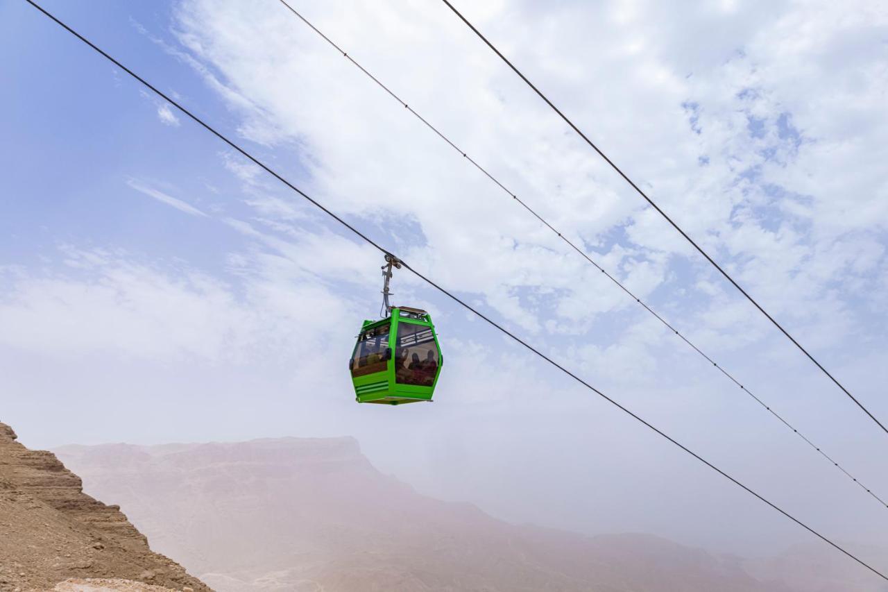 Tolip Resort El Galala Majestic Ain Sukhna Exterior foto The photo shows a green cable car suspended in the air, traveling along overhead cables. The backdrop features a hazy landscape, likely mountainous or elevated terrain, with a cloudy sky. The scene suggests a scenic transportation method, possibly us