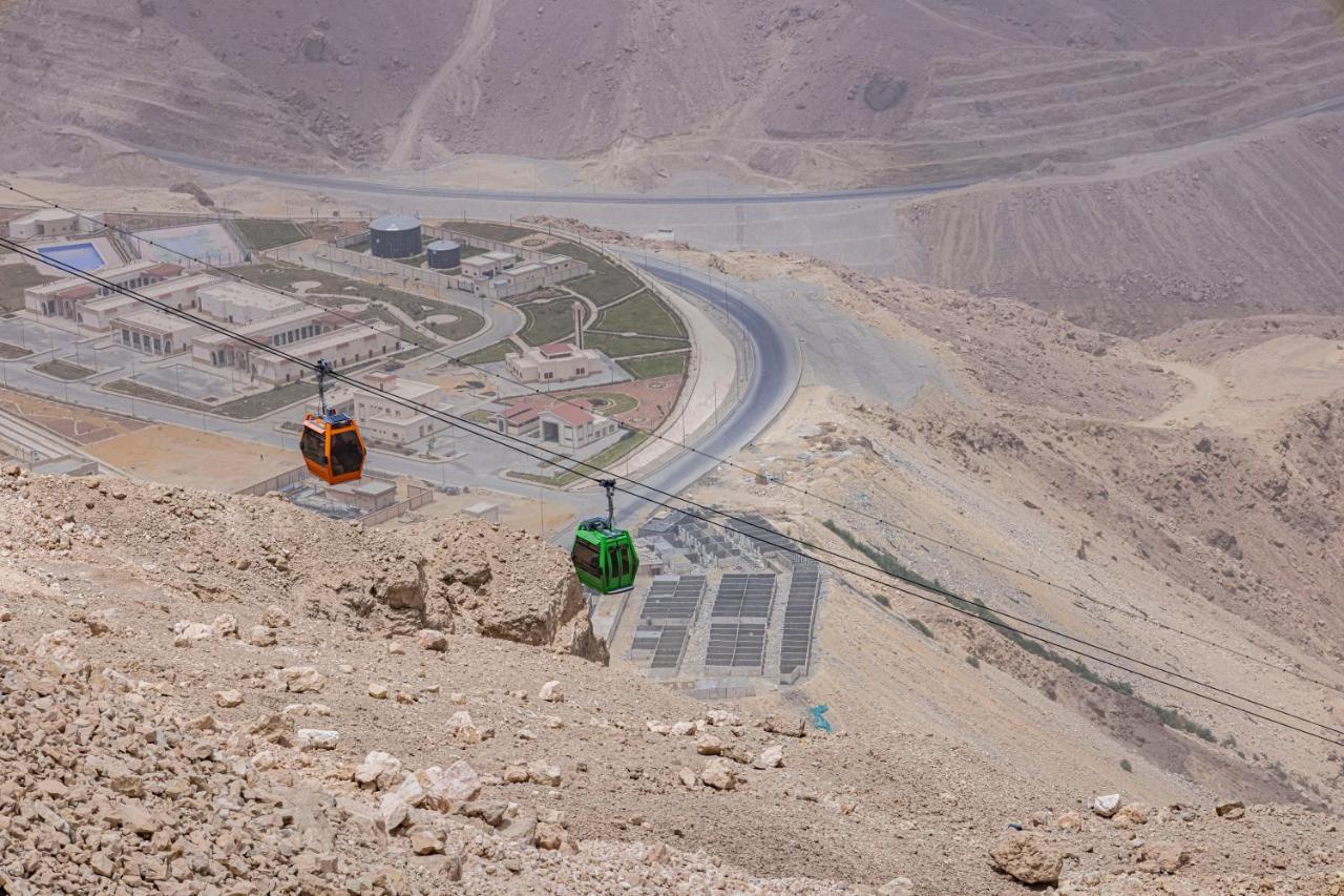 Tolip Resort El Galala Majestic Ain Sukhna Exterior foto The photo shows a scenic view from a high elevation, featuring a cable car system. Two cable cars are visible, one orange and one green, traveling along cables down the mountainside. Below, there appears to be a developed area with roads and light st