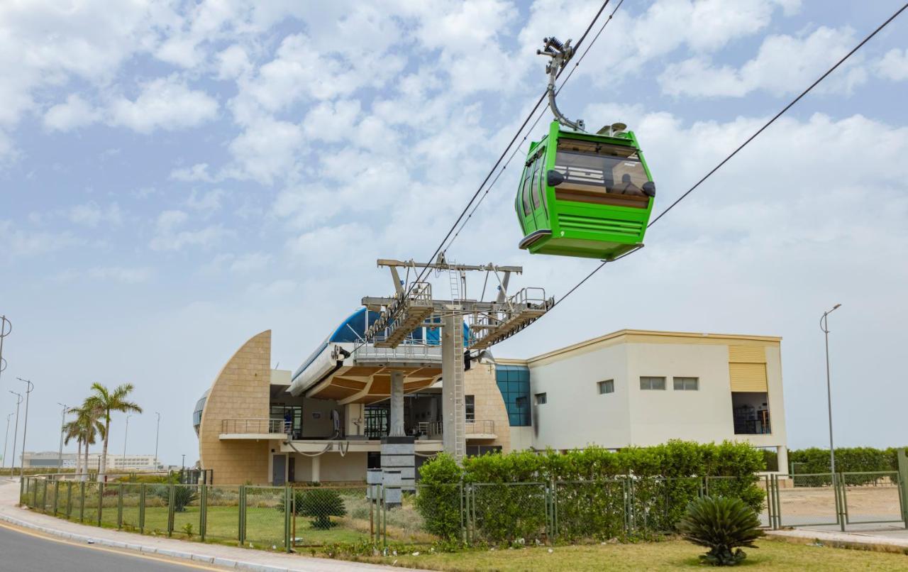 Tolip Resort El Galala Majestic Ain Sukhna Exterior foto The photo shows a cable car or gondola system in operation, featuring a green-colored gondola. It is suspended from cables and moving towards a station, which appears to be a modern building with a unique architectural design. The station has large w