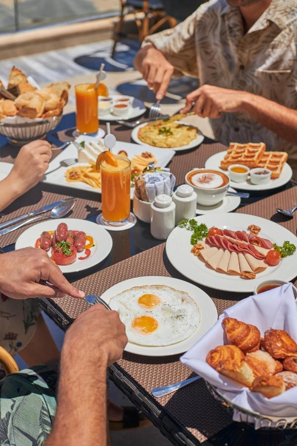 Tolip Resort El Galala Majestic Ain Sukhna Exterior foto The photo features a spread of breakfast dishes on a table. There are two sunny-side-up eggs on one plate, surrounded by various food items, including slices of ham, sausages, and fresh tomatoes. Another plate holds a serving of waffles. A bowl with 