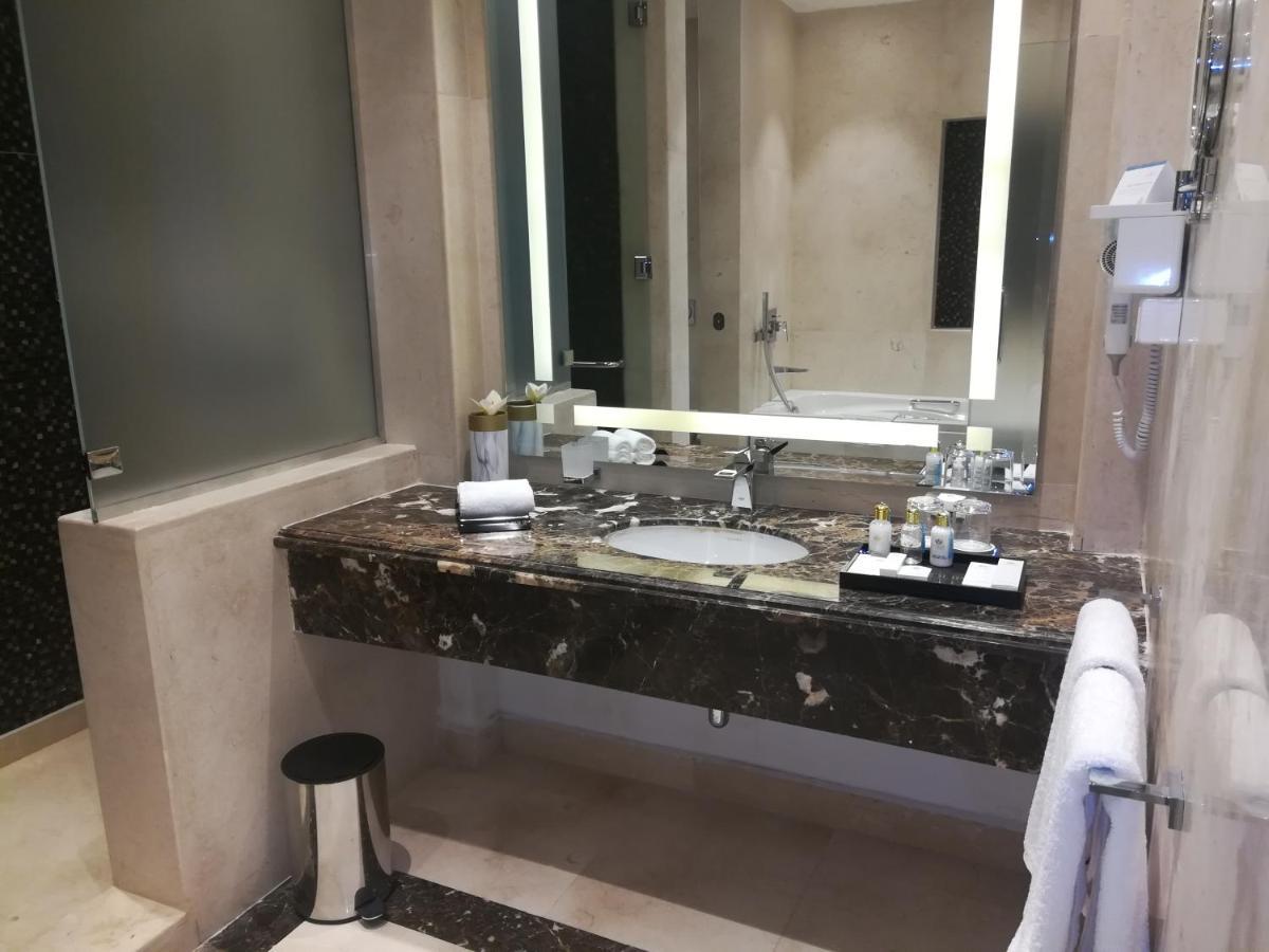 Tolip Resort El Galala Majestic Ain Sukhna Exterior foto The photo shows a modern bathroom with elegant design features. There is a large vanity made of dark marble with a sink and a set of toiletries neatly arranged on top. A mirror with built-in lighting is mounted above the sink. To the side, there is a