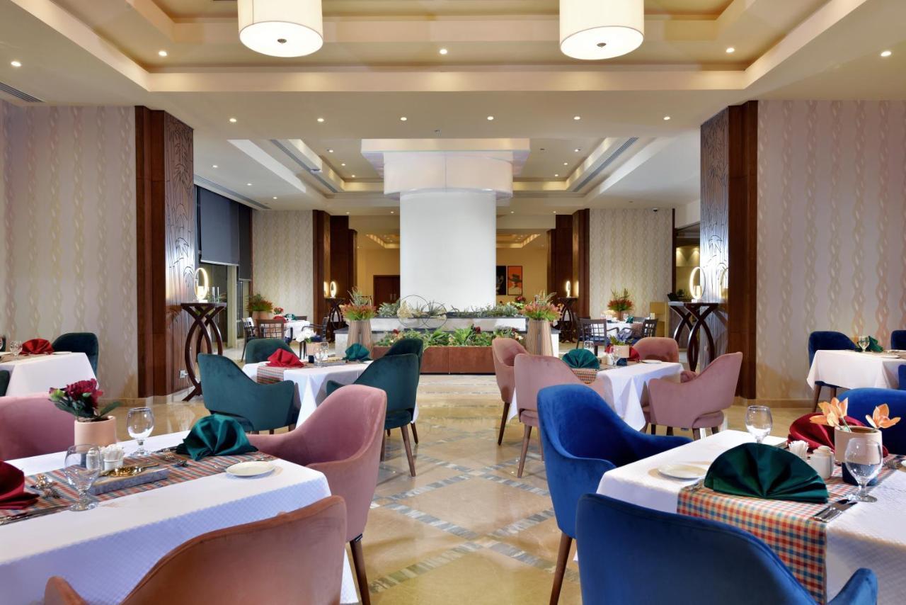 Tolip Resort El Galala Majestic Ain Sukhna Exterior foto The photo shows a spacious and elegantly designed restaurant interior. The layout includes several round tables dressed in white tablecloths, each set with decorative plates, cutlery, and colorful napkins. The chairs are upholstered in a variety of c